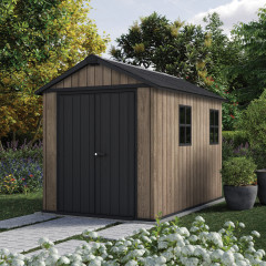Plastový zahradní domek Keter DECO APEX 759/975 Ashwood v barvě imitující dřevo umístěný v zahradní aranžmá