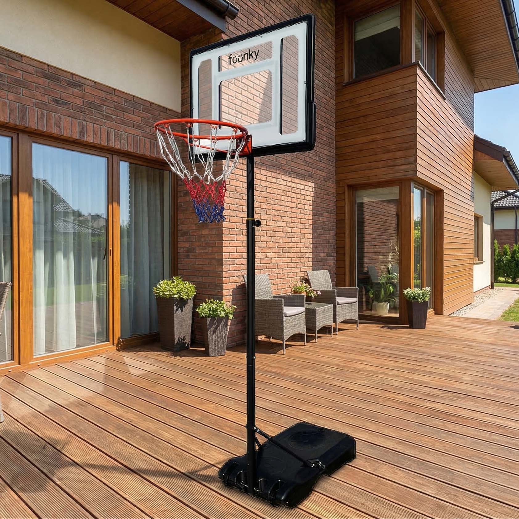 Mobilní basketbalový koš Fuunky 150-210 cm umístěný na dřevěné terase u cihlového domu