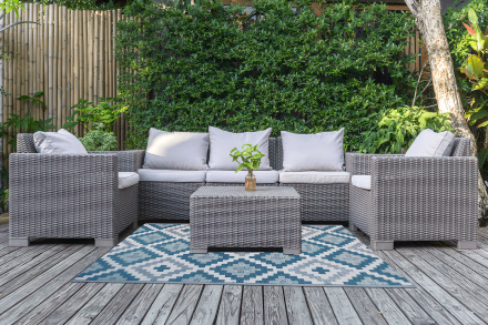 Zahradní koberec na balkon Wires Blue 180x270 cm s modrým geometrickým vzorem rozložený na dřevěné terase před ratanovým nábytkem