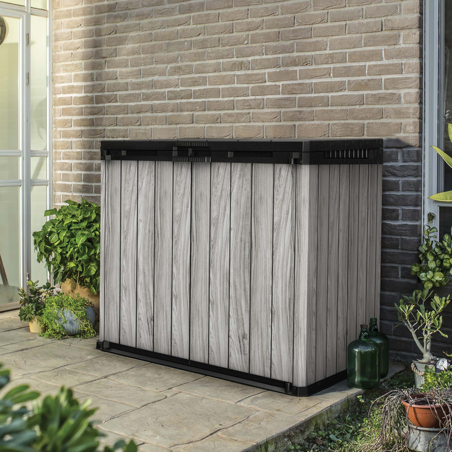 Zahradní úložný box Keter SIO Darwin 1150L v barvě Storm Grey na terase u cihlové zdi