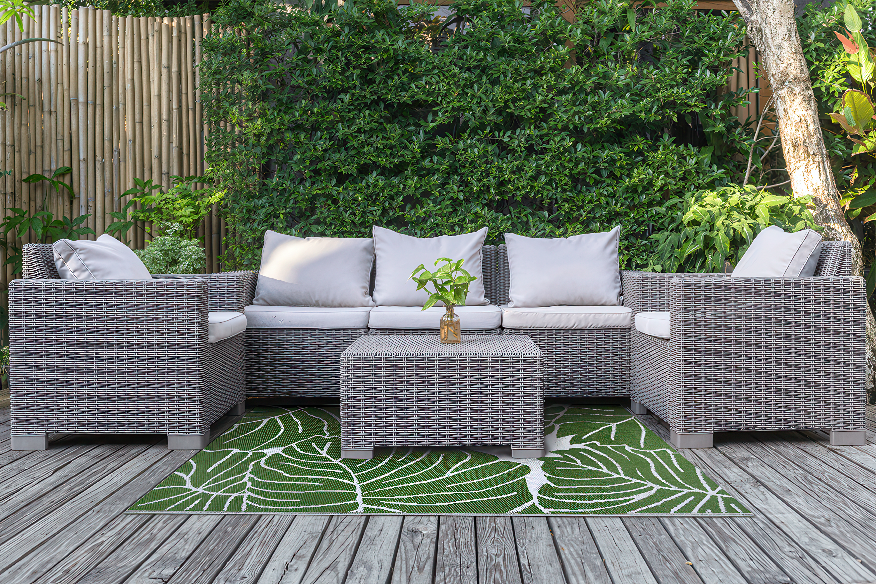 Zahradní a terasový koberec 160x230 cm Monstera MOODME na dřevěné terase pod ratanovým zahradním nábytkem