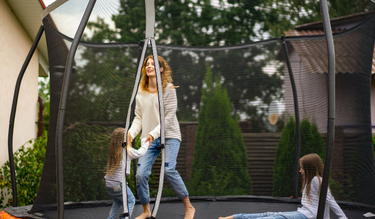 žena sk&aacute;kaj&iacute;c&iacute; s dcerami na zahradn&iacute; trampol&iacute;ně