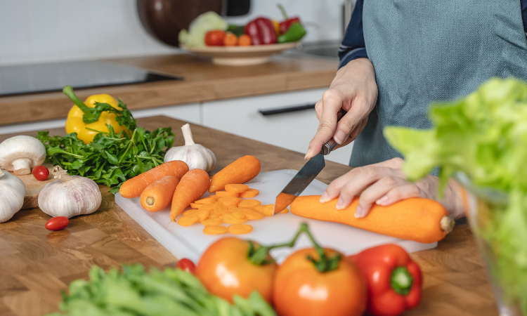 Dom&aacute;c&iacute; hospodyně kr&aacute;j&iacute; mrkev, aby připravila ingredience na obědov&yacute; sal&aacute;t v kuchyni