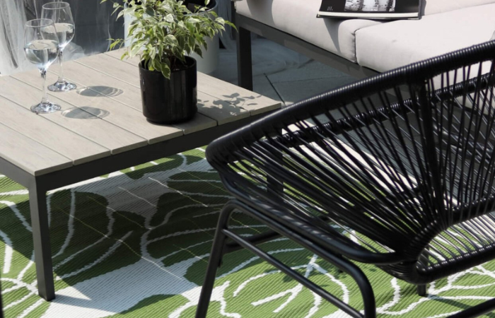 zelen&yacute; venkovn&iacute; koberec s b&iacute;l&yacute;mi monstera listy položen&yacute; pod čern&yacute;m n&aacute;bytkem na balk&oacute;ně