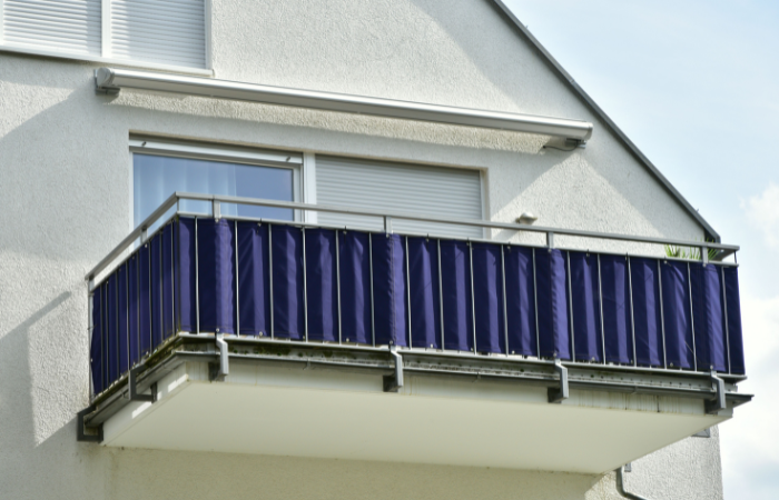 Balkon s kvalitn&iacute;m ocelov&yacute;m z&aacute;bradl&iacute;m v obytn&eacute; budově s tmavě modrou balkonovou z&aacute;stěnou