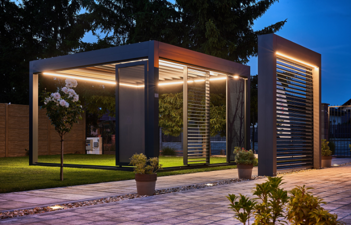 pergola ogrodowa z przepięknym oświetleniem i kompletem akcesri&oacute;w w postaci rolety opuszczanej i paneli żaluzjowych na ścianach bocznych 