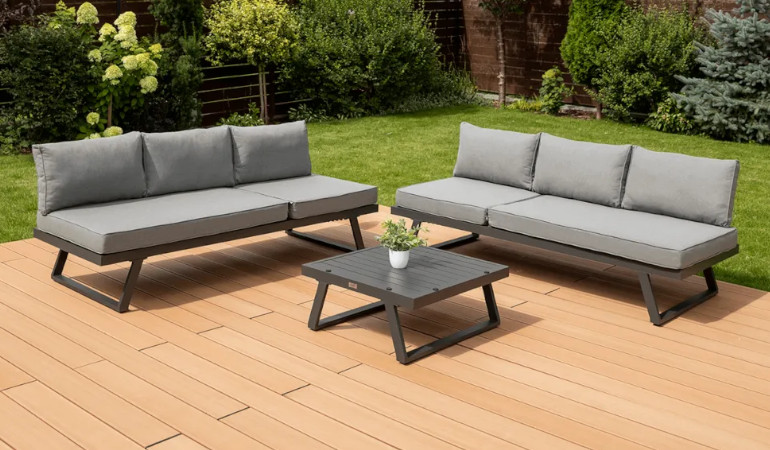 Modul&aacute;rn&iacute; rohov&aacute; skř&iacute;ňka MIDWAY Dark Grey - FOCUS GARDEN na zahradn&iacute; terase obklopen&eacute; zelen&iacute;, koutek je v &scaron;ed&eacute; barvě a je vybaven stolem.