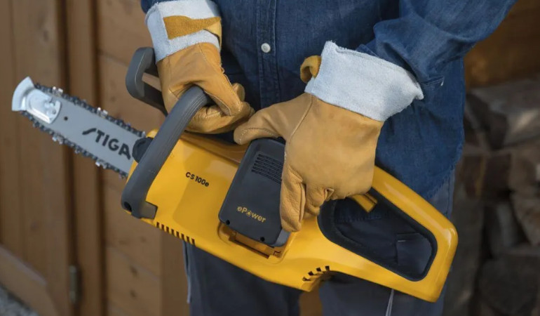 Muž drž&iacute; ve žlut&yacute;ch rukavic&iacute;ch akumul&aacute;torovou řetězovou pilu CS 100E 2,0Ah, řada 100 od společnosti Stiga.
