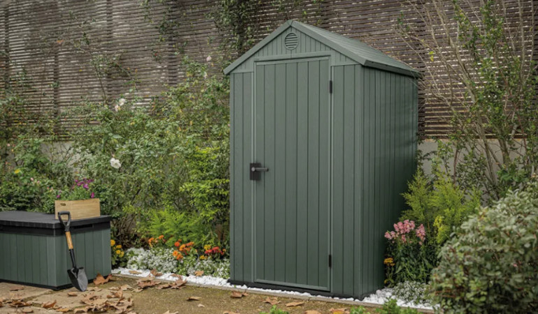 Zahradní domek DARWIN 4x4 zelený - Keter na zahradě pod plotem obklopený zelení a květinami