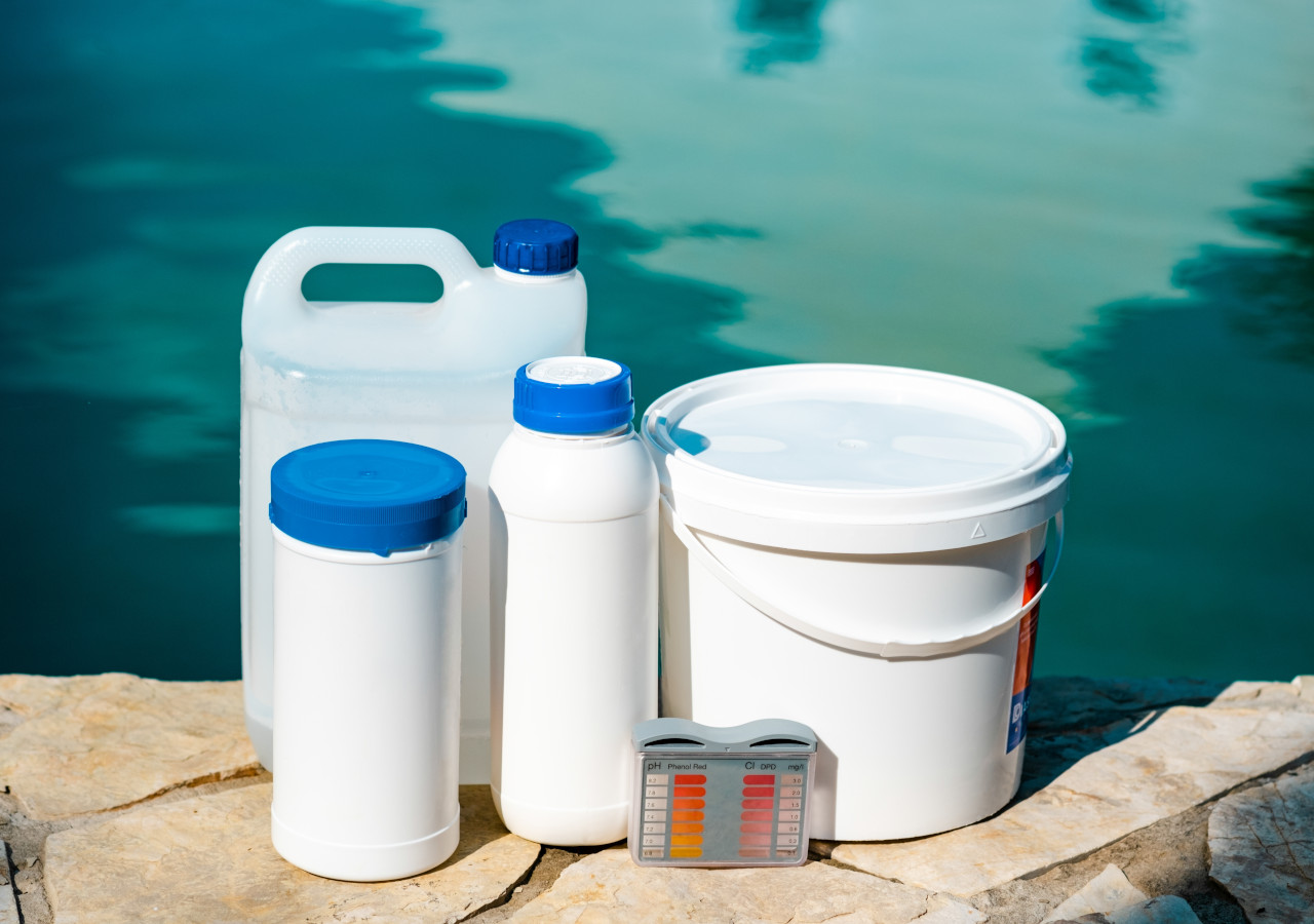 Preparaty chemiczne w plastikowych opakowaniach ustawione obok basenu z wodą